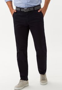 Chinos blu navy con vestibilità slim, in materiale cotone, e una cintura intrecciata nera e grigia. Abbinati a sneakers grigie chiare con accenti sottili.