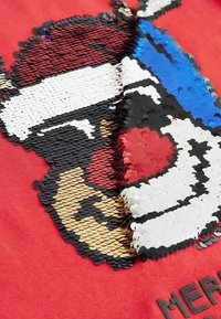 Tissu rouge orné d'un motif en sequins noir, blanc, rouge, bleu et doré, représentant un personnage portant un bonnet de Noël et un nez.