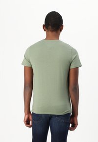 Grön kortärmad t-shirt i bomull, med rund halsringning och en lätt krökt fåll. Bärs tillsammans med mörkblå jeans.