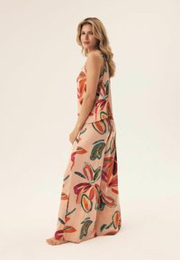 Maxi sukienka z lekkiego materiału, z brzoskwiniowym tłem i dużymi, kolorowymi wzorami kwiatowymi w kolorze czerwonym, zielonym i pomarańczowym.