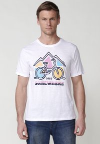 White cotton t-shirt featuring a bicycle graphic with blue, pink, yellow, and black elements. Text reads "LOST SOMEWHERE" in bold letters.