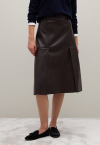 Bruine leren rok met een recht model, voorzien van paneeldetails en een knielengte, gecombineerd met zwarte instapschoenen.