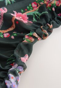 Tessuto in rete verde scuro con motivi floreali in rosa, viola e verde, caratterizzato da arricciature raccolte lungo il bordo.