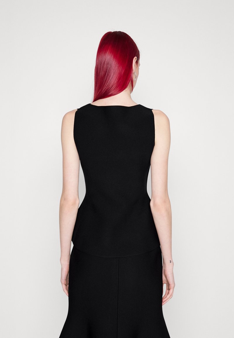 Osoba z długimi rudymi włosami ubrana w dopasowany, czarny top bez rękawów i czarną spódnicę, pokazana od tyłu na jednolitym białym tle.