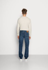 Ljusbeige långärmad skjorta i kombination med mörkblå denimjeans med läderlappar, bakfickor och vita sneakers.