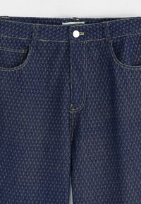 Jean en denim foncé avec un motif de losanges texturé, des coutures contrastées, cinq poches et une fermeture à bouton à la taille.