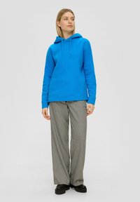 Blauwe capuchontrui met een relaxed fit, gecombineerd met hoog-waist zwart-witte geblokte broek en zwarte chunky schoenen.