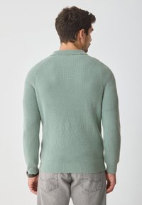 Mint green knitted sweater with ribbed texture, raglan sleeves, and a round neck, paired with light gray jeans.