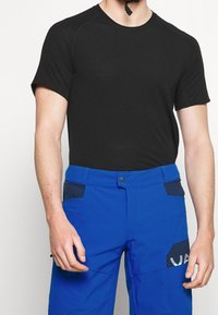 Mustat lyhyet hihattomat t-paidat yhdistettynä kirkkaan sinisiin housuihin, joissa on erottuva tummansininen tasku, napillinen sulkija ja sivutaskut.