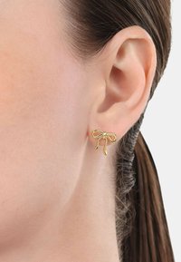 Orecchini a forma di arco in oro con una finitura liscia, caratterizzati da anelli allungati e un design semplice, indossati nel lobo dell'orecchio.