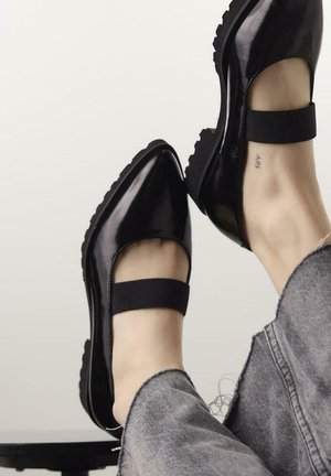 Scarpe in pelle lucida nera con punta affusolata, dotate di un'ampia fascia elastica attorno alla caviglia e suola in gomma testurizzata.
