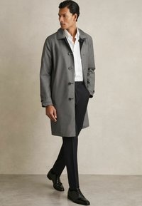 Palton gri cu gât, asortat cu o cămașă albă și pantaloni negri. Pantofi din piele negri completează ținuta. Textură netedă.