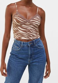 Camisola cropped a zebra in tonalità marrone e beige con bordi in pizzo, indossata con jeans blu a vita alta; il tessuto appare a costine e aderente.