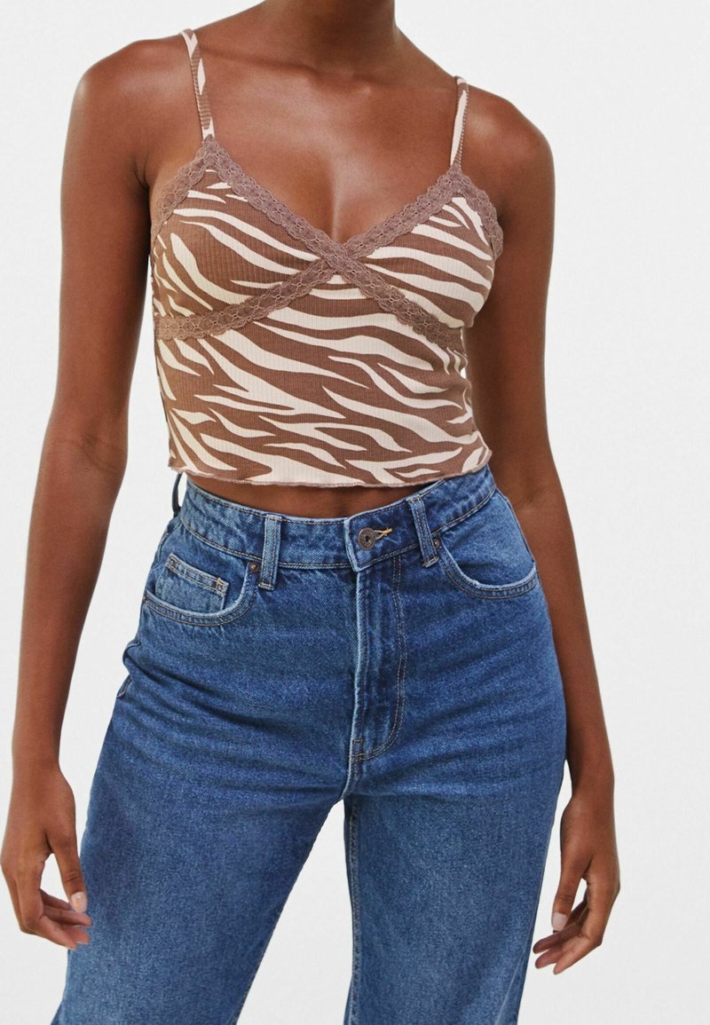 Camisola cropped a zebra in tonalità marrone e beige con bordi in pizzo, indossata con jeans blu a vita alta; il tessuto appare a costine e aderente.