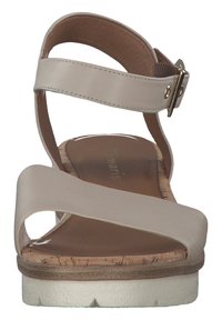 Sandales beiges à lanières avec une semelle en liège, un matériau supérieur doux, une sangle de cheville réglable avec des éléments en or, et une semelle blanche texturée.