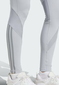 Lichtgrijze sportleggingen hebben een aansluitend ontwerp met textuurpanelen en drie verticale grijze strepen aan de buitenkant.