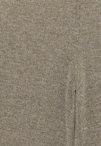 Gros plan d'un tissu tricoté beige avec une couture verticale visible et une petite ouverture fendue sur le côté droit.