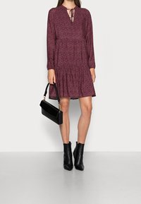 Mörkröd klänning med volangkjol, långa ärmar och en knytning vid halsringen. Matchad med svarta kängor och en svart handväska.