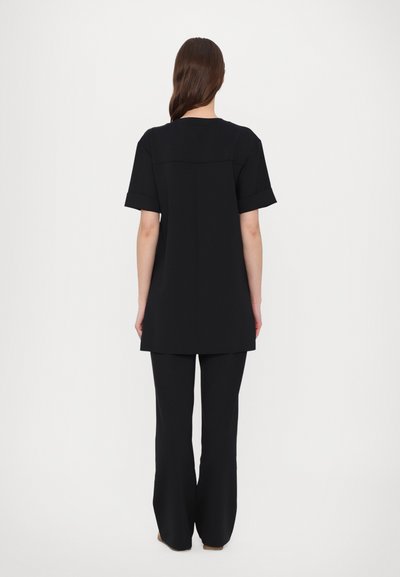 Fekete tunika felső rövid felgöngyölt ujjakban, egyenes szabású, hátoldali varrás részlettel, hozzá illő, magas derekú nadrággal párosítva.