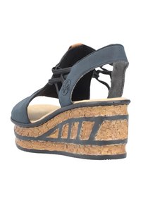 Black suede wedge sandal with cork platform. Features open toe, crisscross straps, and a textured rubber sole with a design accent.