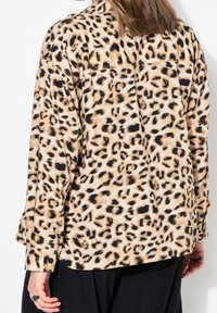 Leopard print shirt featuring a beige background with black spots, long sleeves, and a relaxed fit. Textured fabric with button details.