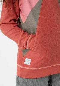 Hoodie en polaire avec des panneaux géométriques rose, rouille et gris. Il présente une poche avant, un ourlet côtelé et une étiquette avec le logo en bas. Texture douce.