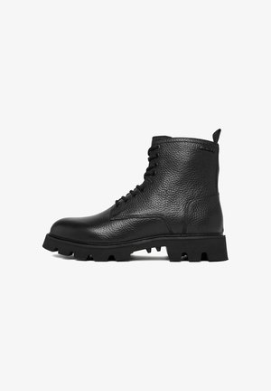 Czarny teksturowany skórzany but typu combat z grubą podeszwą z bieżnikiem, z przodu sznurowany, na wysokości kostki, z pętelką z tyłu.