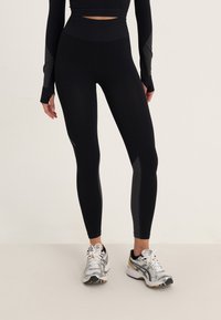 Czarne legginsy sportowe z wysokim stanem, z siateczkowymi akcentami po bokach oraz gładkim, elastycznym materiałem dla wygody.