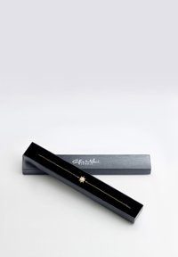 Bracciale oro con un ciondolo a stella, presentato in una scatola nera con una finitura liscia e un marchio bianco sul coperchio.