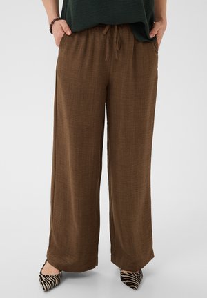 Femeie purtând pantaloni lenjeri maro largi, cu talie elastică și șnur, asortați cu pantofi ascuțiți cu imprimeu de zebră alb-negru.