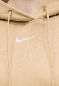 Sweat à capuche beige avec logo Nike swoosh blanc brodé sur la poitrine, doté de cordons assortis et d'œillets en métal.