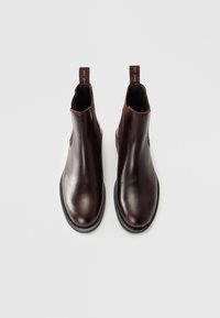 Pair of dark brown leather Chelsea boots with black soles and elastic side panels, viewed from above on a light background.