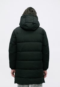 Chaqueta de plumas negra con capucha, que presenta un diseño acolchado, una silueta larga y puños elásticos. El material parece suave e insulated.