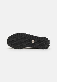 Suela de zapato de goma negra con un patrón de agarre texturizado y un detalle de Hardware circular en el centro, diseñado para ofrecer tracción y durabilidad.