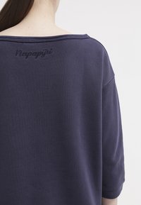 Maglione oversize blu navy con tessuto strutturato. Presenta un'ampia scollatura e il logo "Napapijri" ricamato sul retro. Maniche corte.