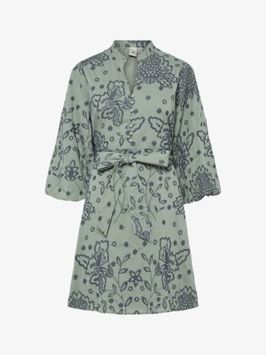 Šviesiai žalia trumpomis rankovėmis su tamsiai mėlynomis gėlėmis siuvinėjimu, mygtukais užsegama priekyje, stovinčiu apykakle ir juosmeniu su raišteliu, leidžiančiu reguliuoti pritaikymą.