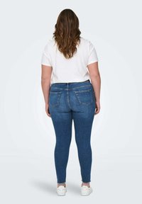 Jean skinny en denim bleu foncé, taille haute avec poches, légère décoloration à l'ourlet. Associé à un t-shirt blanc uni et des baskets blanches.