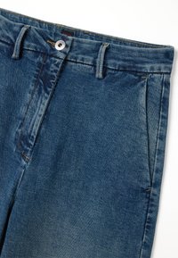 Jeans de mezclilla en un lavado azul medio con un corte estándar. Incluye bolsillos laterales, pasadores para cinturón y un cierre de botón metálico.