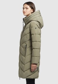 Abrigo tipo puffer verde oliva con capucha, que presenta un patrón de chevrón, cierre frontal y bolsillos laterales, fabricado con un tejido ligero y texturizado.