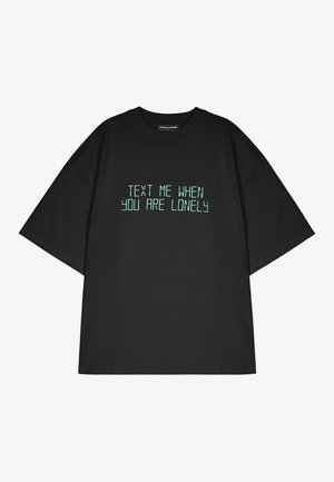 Black oversized t-shirt made of cotton featuring green printed text that reads "TEXT ME WHEN YOU ARE LONELY." Short sleeves, standard crew neck.