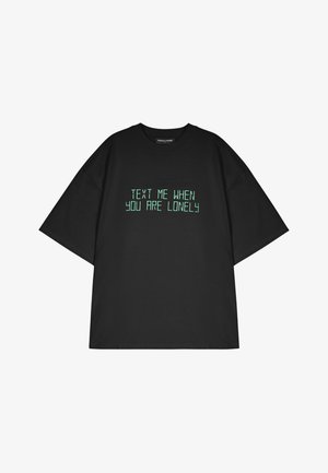 T-shirt oversized preta em algodão com texto impresso em verde que diz "MANDA-ME MENSAEM QUANDO ESTIVERES SOZINHO." Mangas curtas, decote redondo standard.