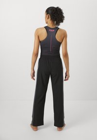 Svart tanktopp med rosa detaljer og racerback-design, kombinert med løse svarte bukser med sidestriper og elastisk midje.
