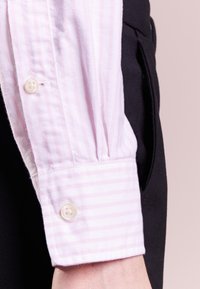 Ljusrosa randig skjortärm med knappstängning, som har en jämn textur och diskret veckning, i kombination med mörk tyg bredvid.