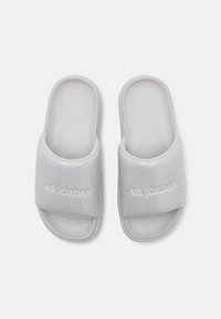 Hvite Air Jordan flip-flops har et blankt stropp med preget logo, formet fotbed, strukturert mønster og flat såledesign.
