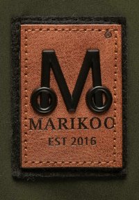 Bruine leren patch met zwart reliëf "M" en cirkels, met "MARIKOO" en "EST 2016" in vetgedrukte letters, gestikt op een donkere stofachtergrond.