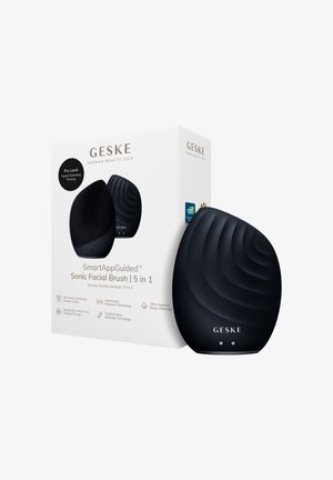 Brosse faciale sonique noire GESKE avec surface texturée à côté d’une boîte blanche indiquant le nom du produit et ses fonctionnalités pour un nettoyage en profondeur et un massage.