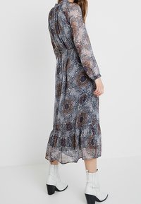 Lange, doorschijnende jurk met een bloemenpatroon in blauw, bruin en wit. Heeft lange mouwen, een hoge halslijn en een ruchesrand. Gekocht met witte laarzen.