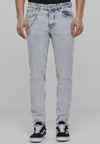 Heledad hallhalli denimhämbud, millel on kitsas lõige, kettkaunistusega ja mitme taskuga. Kombineeritud mustade ja valgete tennisetega.