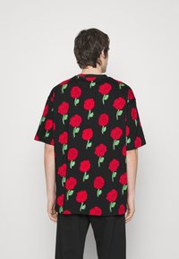 Krátký rukáv, černé tričko s vzorem červených růží, se zelenými stonky a listy, uvolněný střih a měkká textura látky.