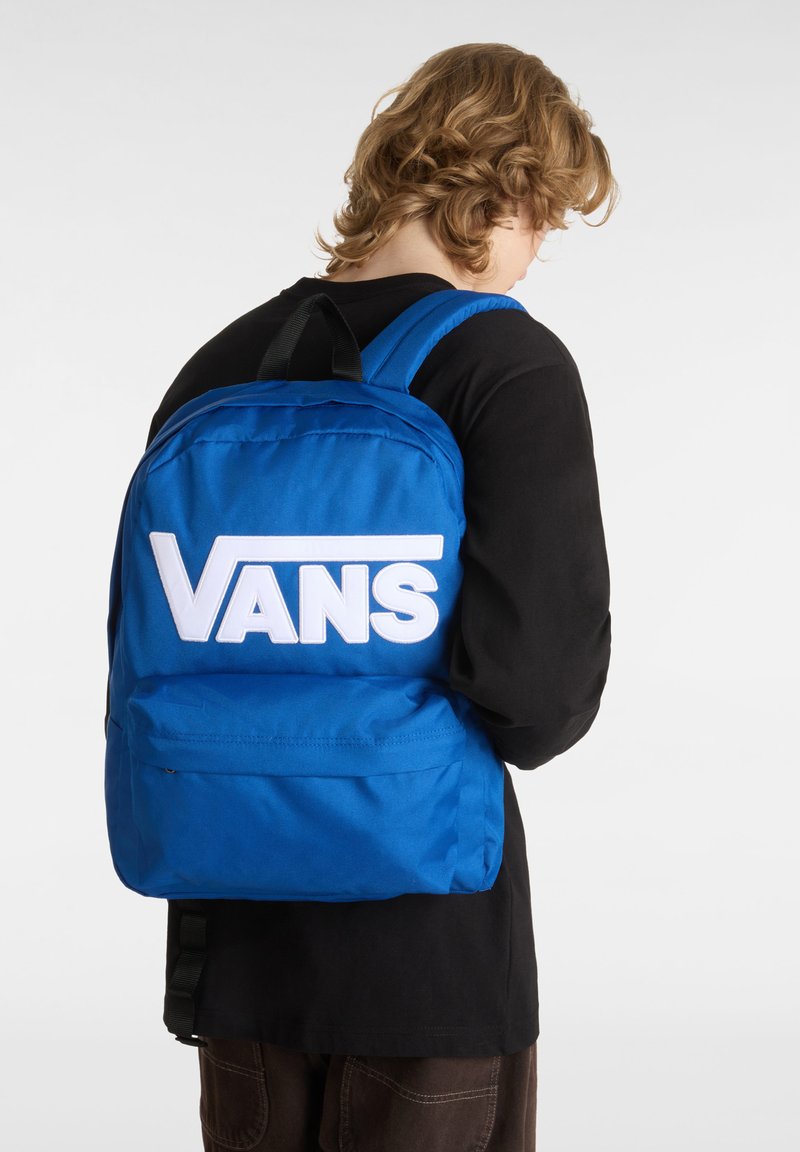 Zaino blu in tessuto, con un grande logo bianco "VANS", due spallacci e una tasca frontale. Design semplice e rettangolare.